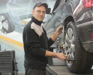 Leistungen Mechanic performing wheel alignment on a car in a professional garage setting.